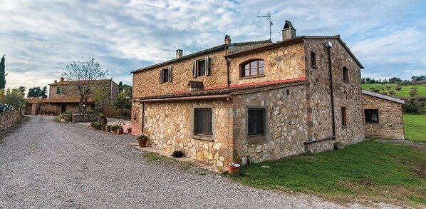 Une maison en pierre avec une allée gravillonnée, un petit jardin et un ciel dégagé.
