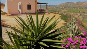 Une maison dotée d’un patio, entourée de plantes et de fleurs, qui offre une vue sur un paysage vallonné.