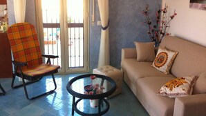 Un salon comprenant un canapé, un fauteuil, une table en verre et une vue sur l’extérieur, visible à travers une porte vitrée.