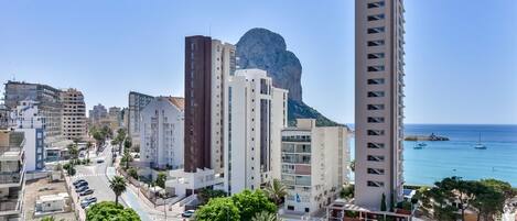 Un paysage urbain côtier avec des immeubles modernes de grande hauteur, une falaise imposante et une vue dégagée sur la mer, où l’on aperçoit des bateaux.