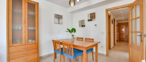 A dining area with a wooden table and chairs, a cabinet with glass doors, and a hanging light fixture.