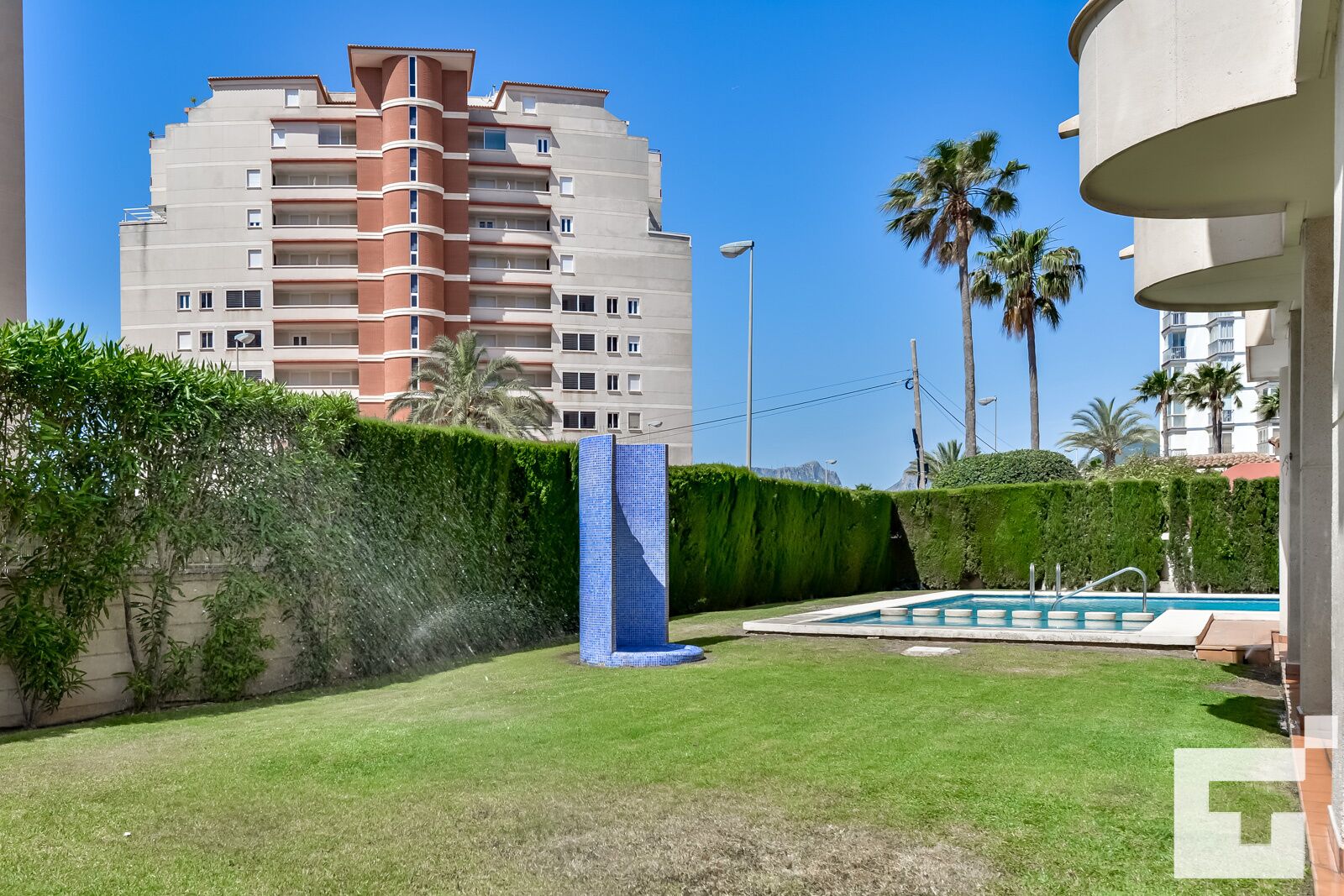 Un edificio residencial con piscina, césped verde y palmeras.