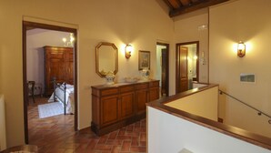 Um corredor com escada de madeira, espelho e arandelas.