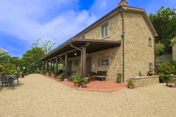 A stone building with a covered patio, outdoor seating, and potted plants.