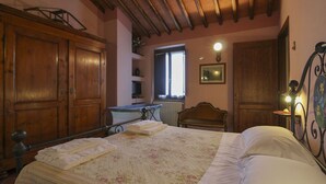 Quarto com cama de madeira, radiador, janela e luminária fixada na parede.