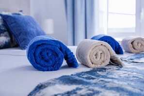 A neatly made bed with rolled towels in blue and beige colors.