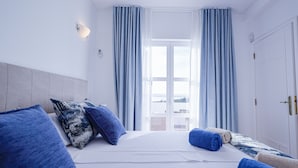 A hotel room with a large bed, blue and white pillows, a white headboard, and a view of the outside through a window with blue curtains. - Villa w/private pool in peaceful holiday complex (Albufeira)