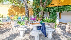 An outdoor seating area with tables and chairs, surrounded by plants and trees.