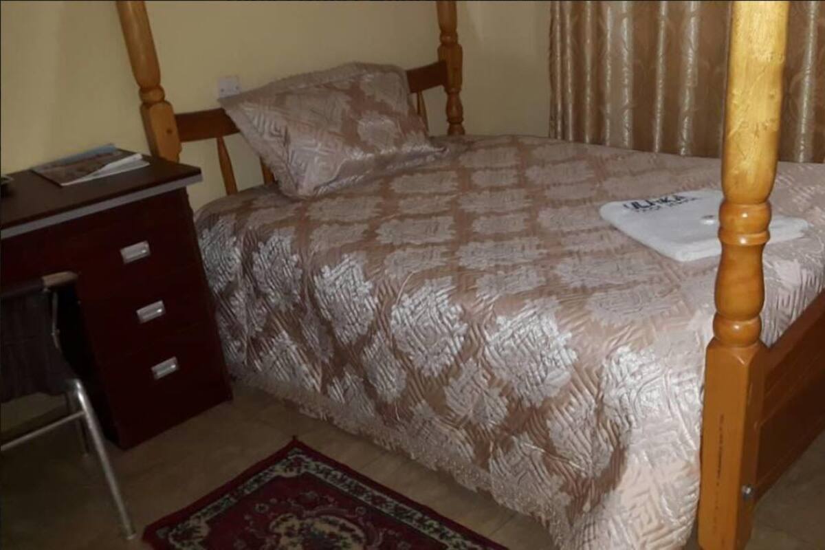 A bedroom with a wooden four-poster bed, a red dresser, and a patterned bedspread.