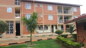 A multi-story building with a brick facade, balconies, and a small courtyard with palm trees and shrubs. - Ulrika Guest House (Entebbe)