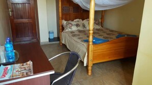A room with a wooden bed, a desk with a chair, a water bottle, and a trash bin. - Ulrika Guest House (Entebbe)