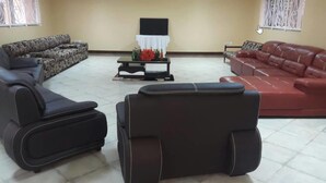 A living room with a sofa set, a coffee table with flowers, and a TV on a stand. - Ulrika Guest House (Entebbe)