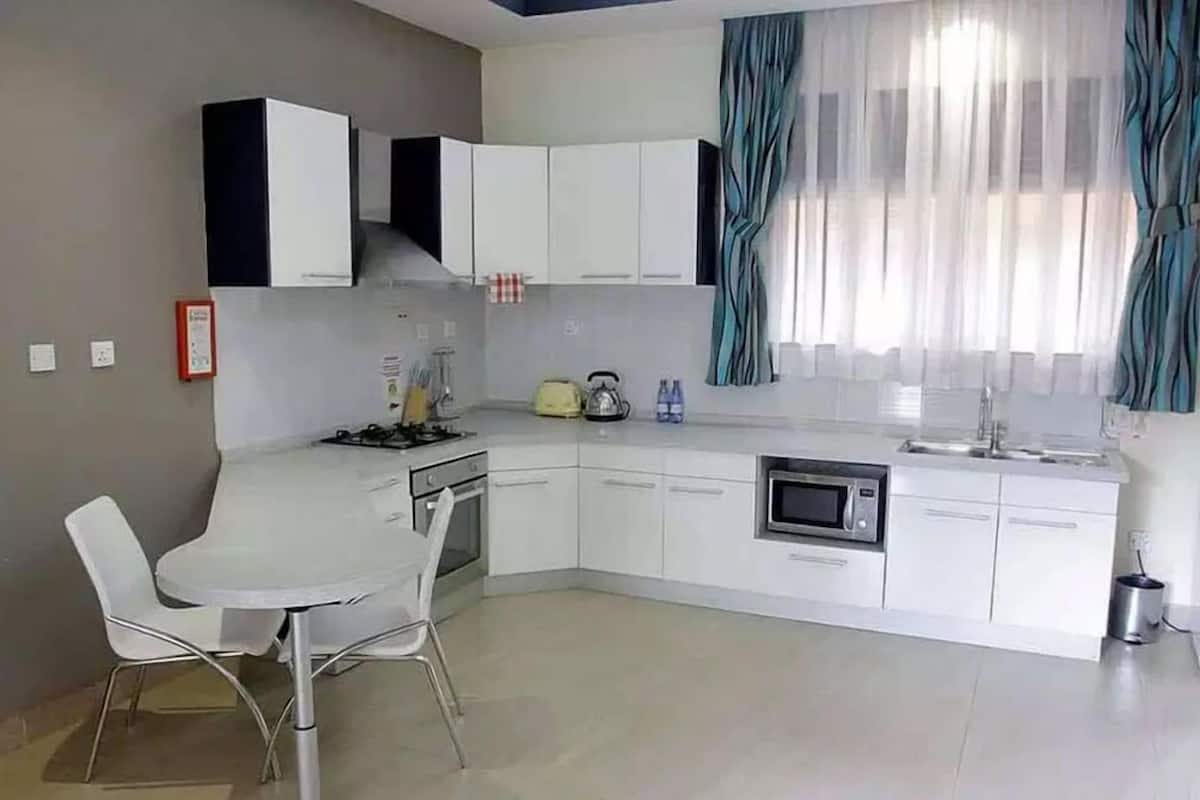 A modern kitchen with white cabinets, a dining area with two chairs, a microwave, and a kettle.