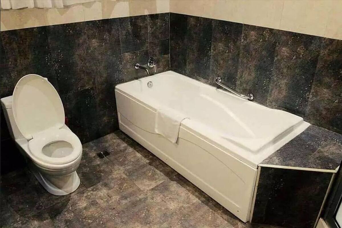 A bathroom with a toilet, a bathtub, and dark tiled walls.