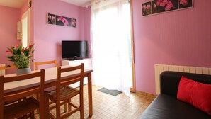 Una habitación con una mesa de comedor, sillas, un televisor, un sofá y una ventana con cortinas.