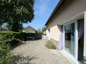 A house with a gravel driveway, a patio with chairs, a thatched-roof structure, and a large sliding glass door.