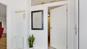 A hallway with a white radiator, a potted plant, a mirror, and a door leading to another room.