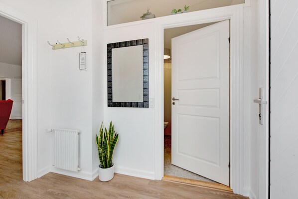A hallway with a white radiator, a potted plant, a mirror, and a door leading to another room. - Årslev B&B (Randers)