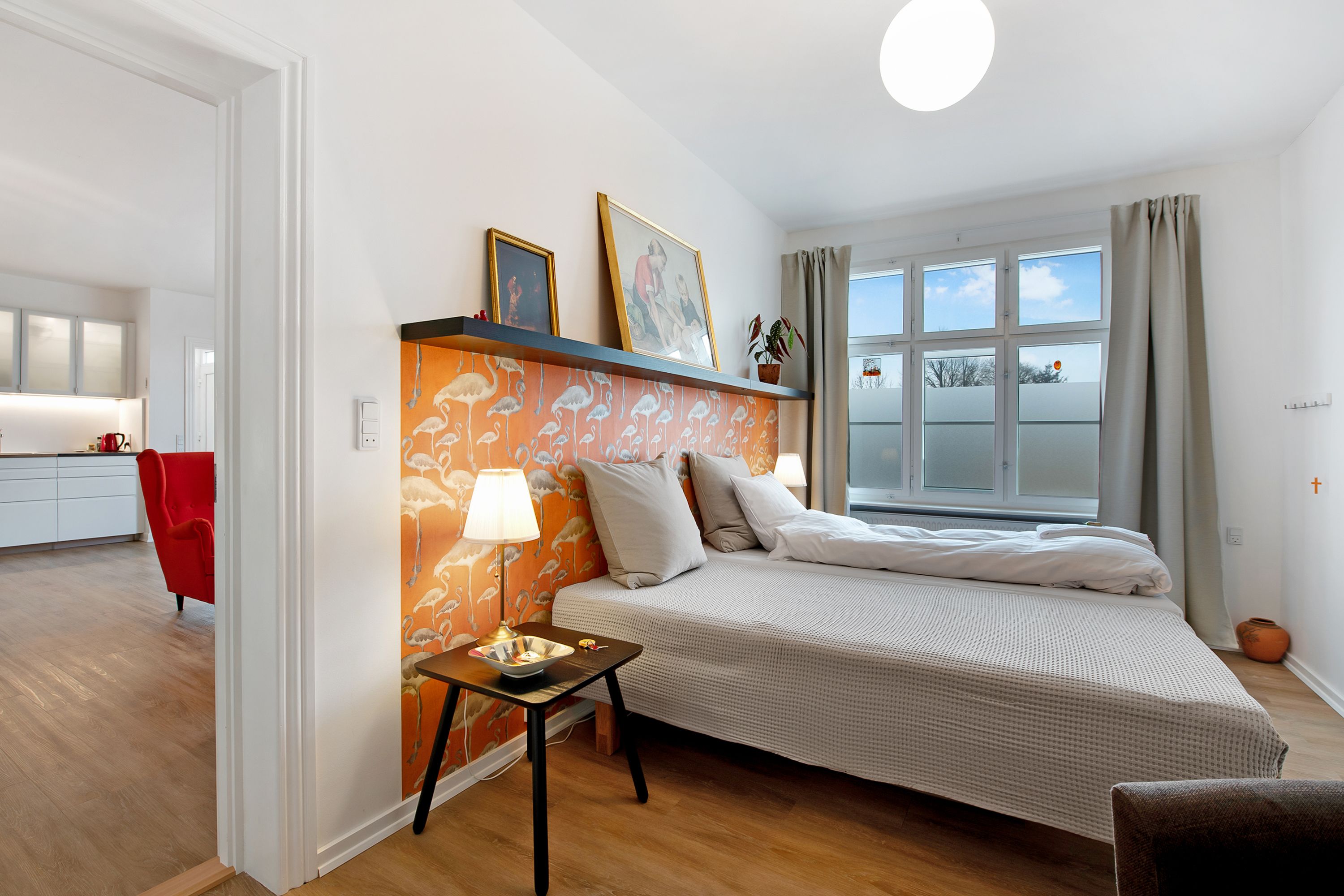 Un dormitorio con cama, mesita de noche, lámpara y ventana con cortinas.