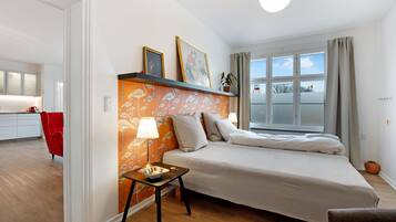 Un dormitorio con cama, mesita de noche, lámpara y ventana con cortinas.