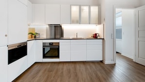 A modern kitchen with white cabinets, a stainless steel range hood, a built-in oven, and a dishwasher.
