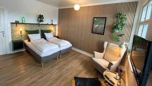 A hotel room with two beds, a sofa, a chair, a small table, a TV, and a window.
