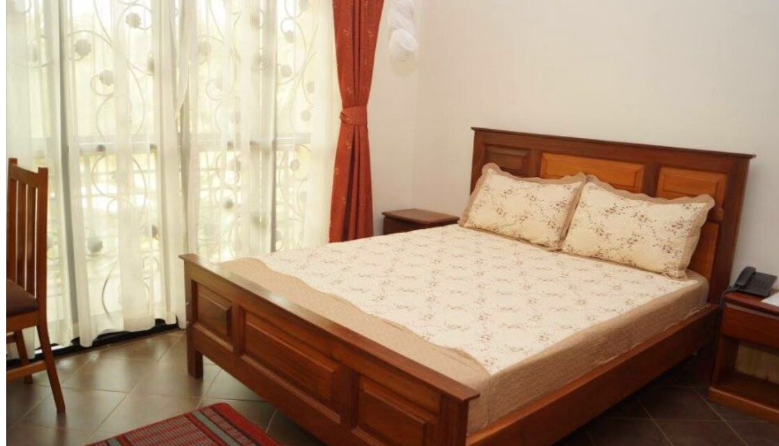 A bedroom with a wooden bed, two pillows, a nightstand, a chair, and a window with curtains.