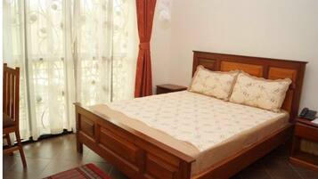 A bedroom with a wooden bed, two pillows, a nightstand, a chair, and a window with curtains.