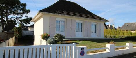 Une maison de plain-pied avec un toit sombre, des murs extérieurs blancs et une clôture blanche à l’avant.