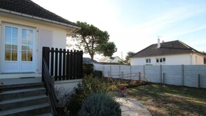 Il s’agit d’une propriété résidentielle comprenant une maison blanche, un chemin en pierre, une clôture en bois et un petit jardin agrémenté d’arbustes et de fleurs.