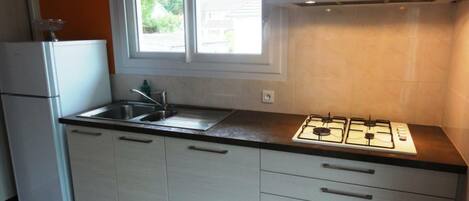 Una cocina compacta con armarios blancos, un lavamanos de acero inoxidable, una estufa a gas y un ventanal sobre el lavamanos.