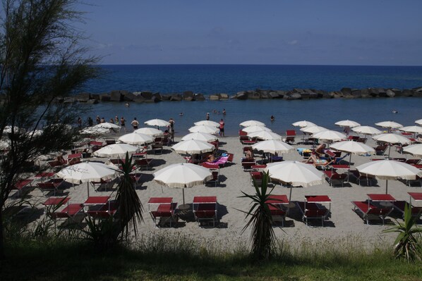 A beach with rows of sunbeds and umbrellas, a rocky breakwater, and the ocean in the background. - Hotel Valeria del Mar (Belvedere Marittimo)