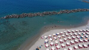 An aerial view of a beach with clear turquoise waters, a rocky breakwater, and numerous sunbeds and umbrellas. - Hotel Valeria del Mar (Belvedere Marittimo)