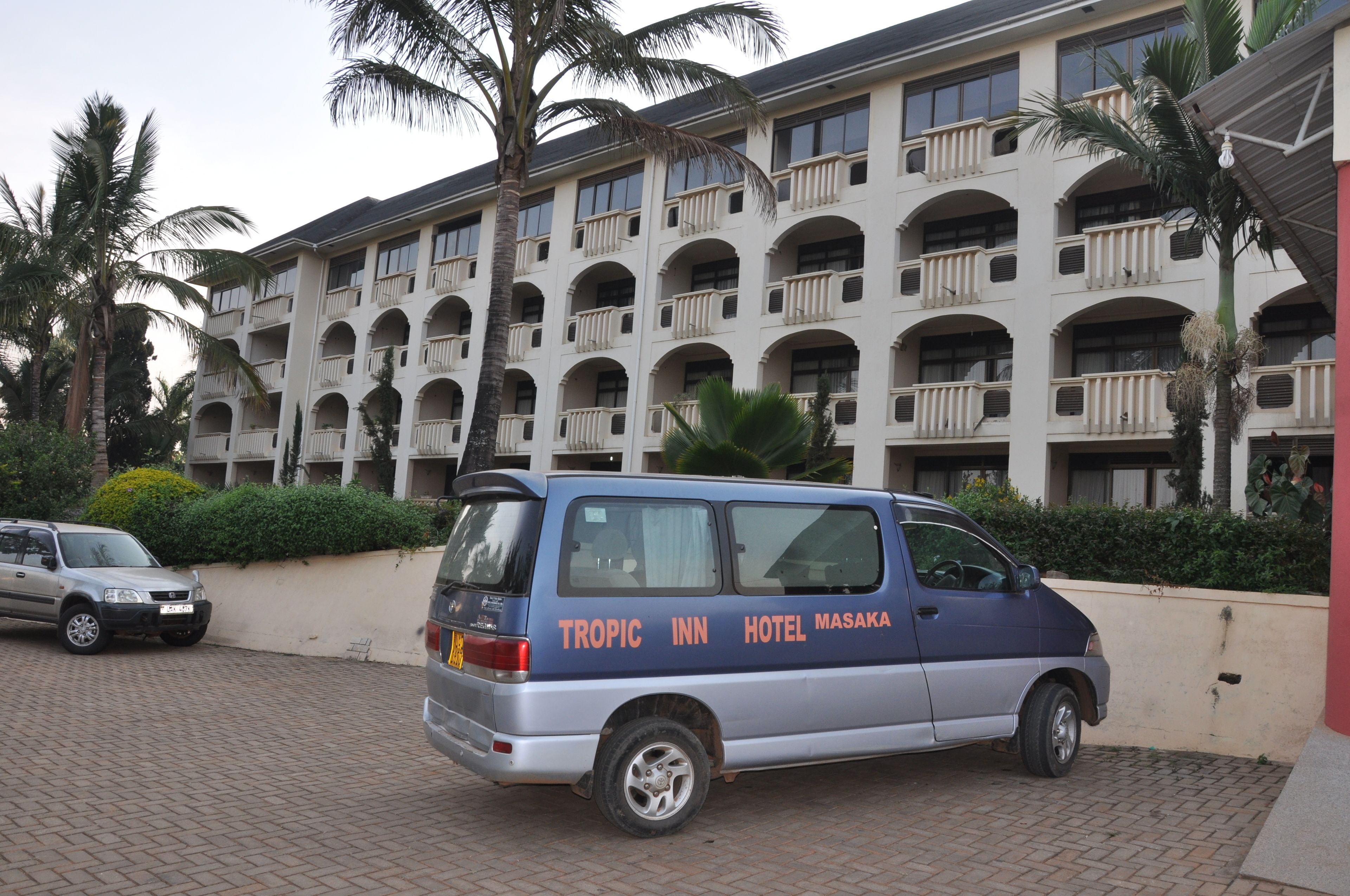 A blue van parked in front of a hotel with multiple balconies and palm trees.