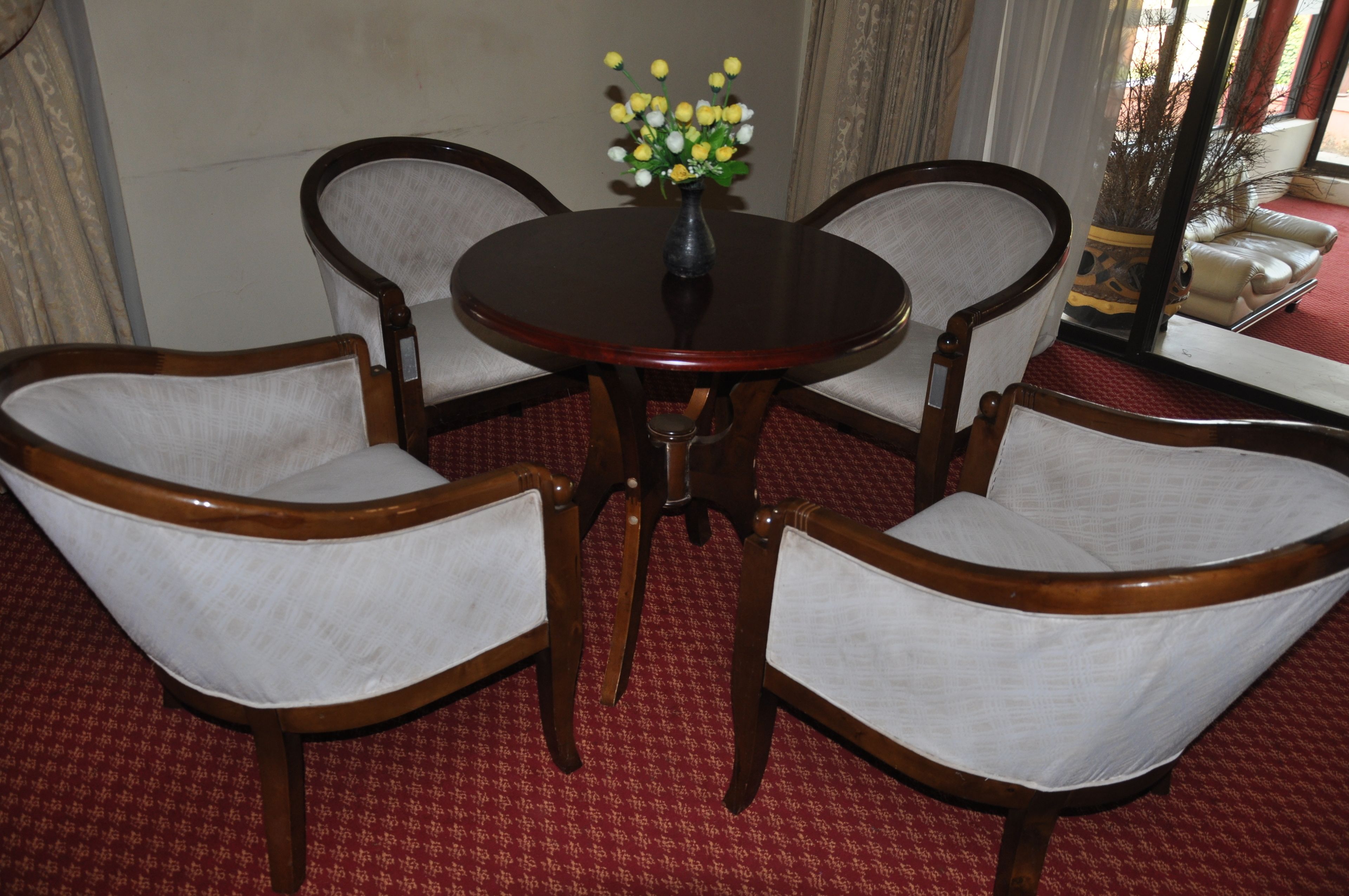 A dining area with a round wooden table and four upholstered chairs. A vase with yellow flowers is placed on the table.