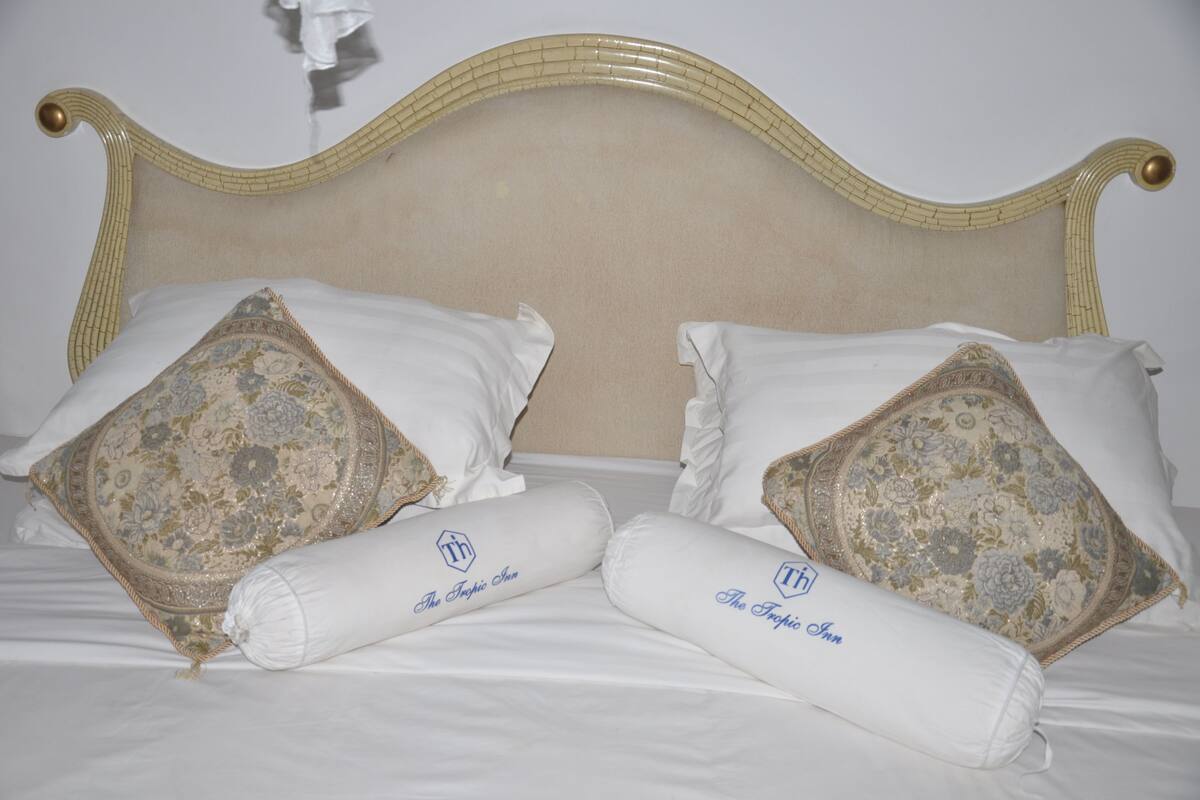 Uma cama com cabeceira, duas almofadas decorativas e dois rolos de toalha com um logotipo.