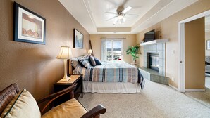 A bedroom with a bed, a nightstand, a chair, a lamp, a ceiling fan, a fireplace, and a view through a glass door. - Beautiful waterfront condo with the boat slip! Its five o'clock somewhere... (Lake Ozark)