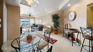 A spacious living area with a glass dining table, a comfortable sofa, a large potted plant, and a wall clock. - Beautiful waterfront condo with the boat slip! Its five o'clock somewhere... (Lake Ozark)