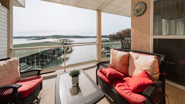 A covered balcony with wicker furniture, a glass table, and a view of a dock and water. - Beautiful waterfront condo with the boat slip! Its five o'clock somewhere... (Lake Ozark)