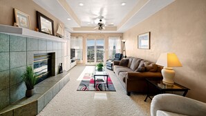 A living room with a fireplace, a sofa, a coffee table, and a view of a lake. - Beautiful waterfront condo with the boat slip! Its five o'clock somewhere... (Lake Ozark)