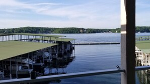 A marina with docked boats and a view of a lake and forested area. - Beautiful waterfront condo with the boat slip! Its five o'clock somewhere... (Lake Ozark)