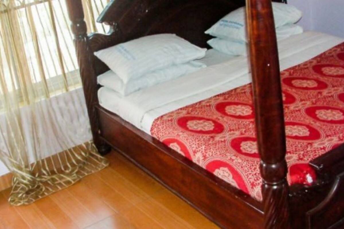 A wooden four-poster bed with white linens and a red patterned bedspread.