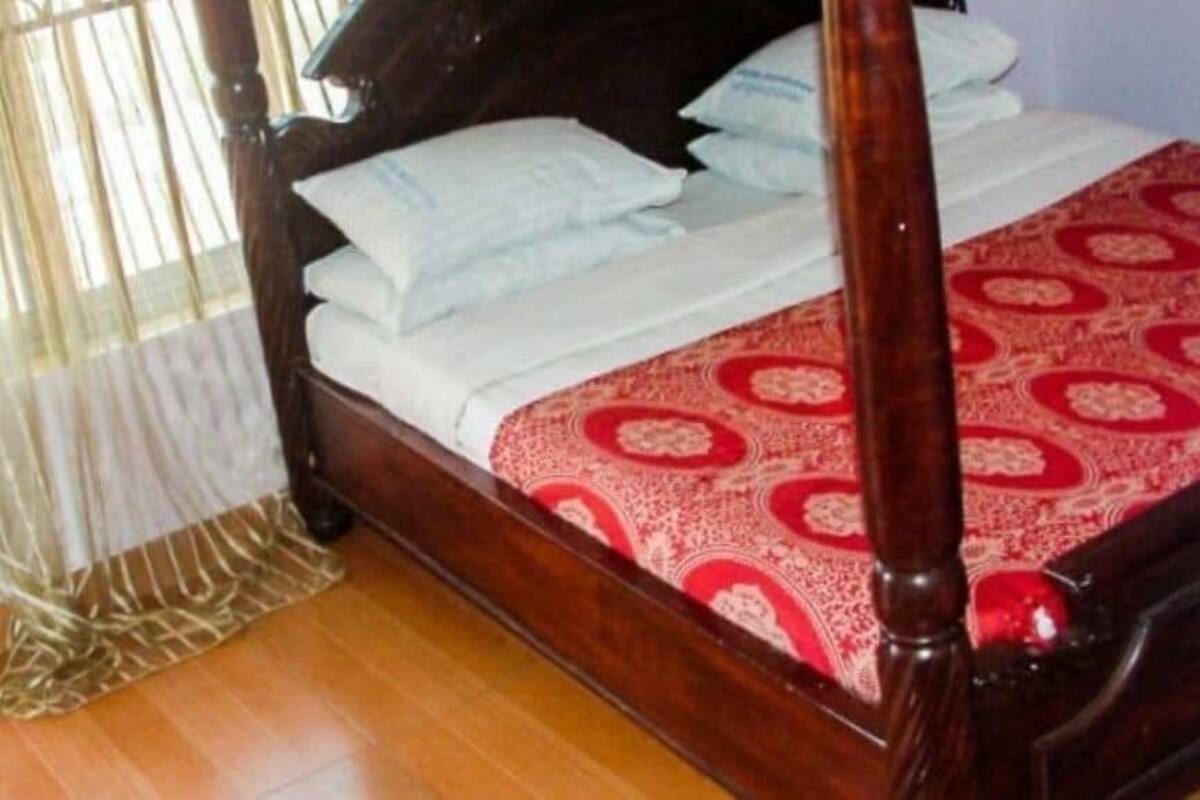 A wooden four-poster bed with white linens and a red patterned bedspread.