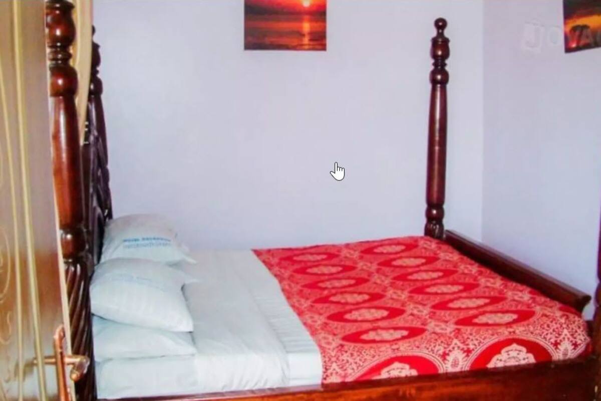 A wooden four-poster bed with white bedding and a red patterned bedspread.