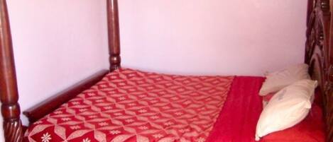 Una cama con dosel con un edredón estampado en rojo y blanco y dos almohadas.