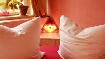 Ein gemütliches Zimmer mit einer roten Couch, weißen Kissen, einem kleinen Tisch mit Topfpflanze und einer dekorativen Leuchte.