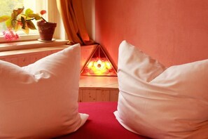 A cozy room with a red couch, white pillows, a small table with a potted plant, and a decorative light fixture. - Spirit Lodge Leipzig - Hostel (Leipzig)