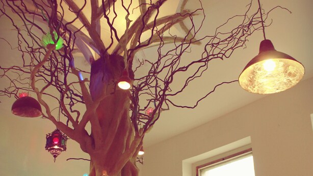A room with a large tree sculpture, a window with a view, and a chair. - Spirit Lodge Leipzig - Hostel (Leipzig)