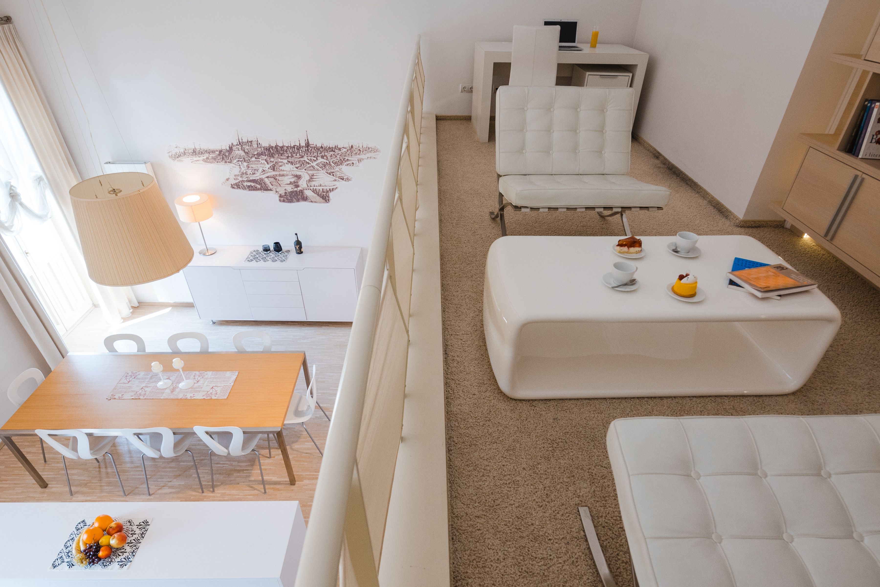 A modern, well-lit living room with a dining area, white furniture, and a cityscape wall art.