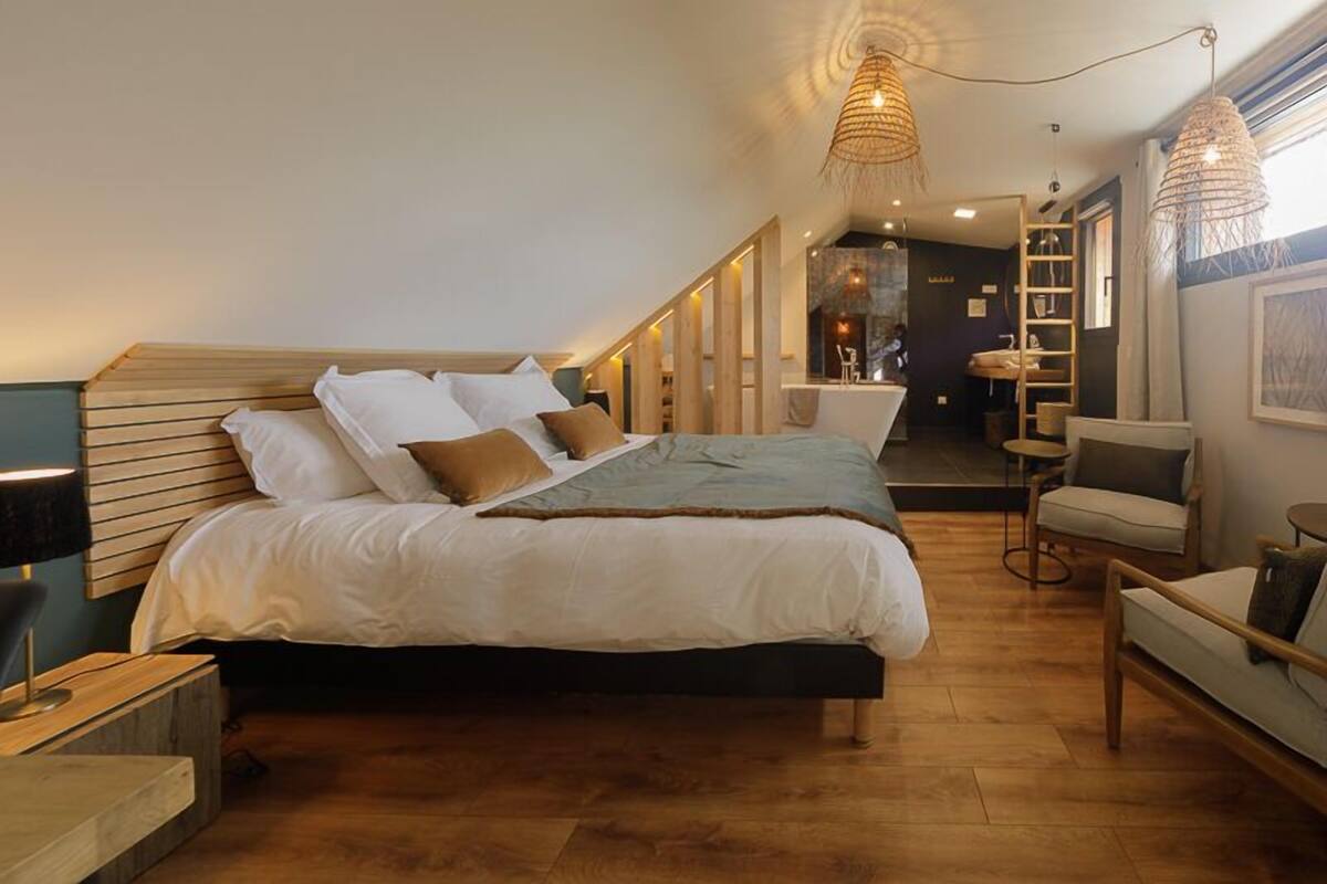 A modern bedroom with a wooden headboard, a large bed with white bedding, a bedside table with a lamp, and a hanging light fixture.